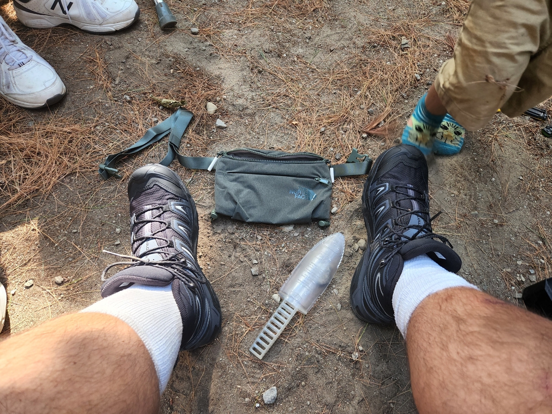 Adam wears his new Salomon hiking boots beside a belt pouch and lightweight poop shovel at camp before the Cascade and Porter hike.