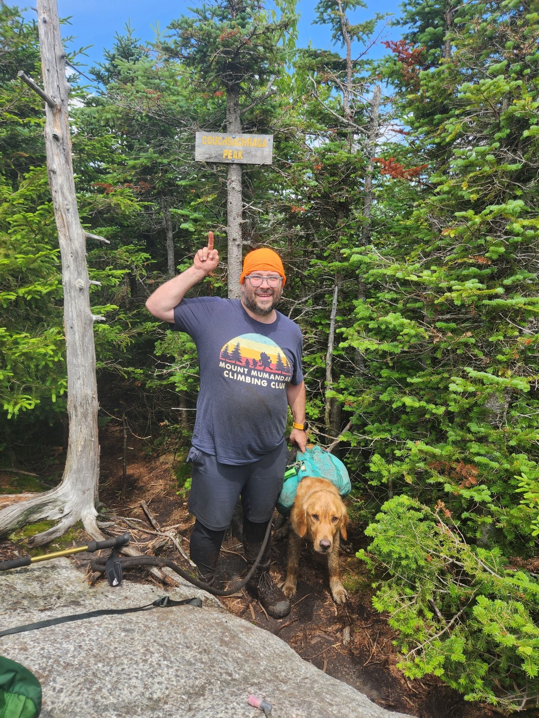 Adam makes a rude gesture while posing with muddy Sunny beneath the Couchsachraga Peak sign.